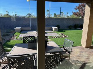 A cozy backyard with a paved patio, modern seating, and artificial turf, ideal for relaxation and outdoor gatherings.