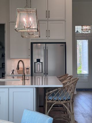 A modern kitchen with sleek pendant lighting, wicker bar stools, and a stainless steel fridge.