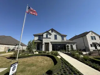 Street view A striking two-story home with a stone facade and lush greenery in Blackhawk by GFO Home (Pflugerville, TX).