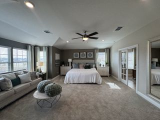 A spacious master bedroom with plush carpeting, a king-size bed, a sitting area with a couch and coffee table, and double glass doors leading to a bathroom.