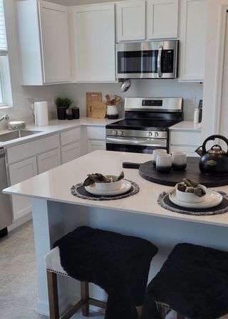 A sleek kitchen features white cabinetry, stainless steel appliances, and a cozy breakfast bar with chic decor.