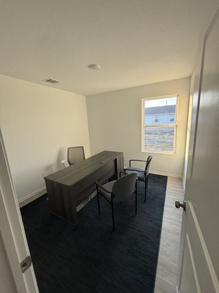 Model Home A bright office space with a dark wood desk, two chairs, and a dark rug, offering a professional setting.