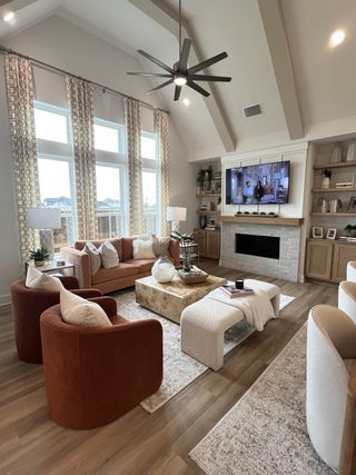 A cozy living room with high ceilings, a stone fireplace, modern furniture, and large windows draped in patterned curtains.