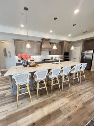 Model Home A modern kitchen with elegant pendant lighting, a large island, wicker barstools, and sleek cabinetry.