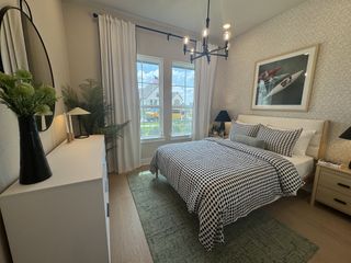 A cozy bedroom with checkered bedding, framed art, and a chic chandelier, featuring lush greenery and natural light.