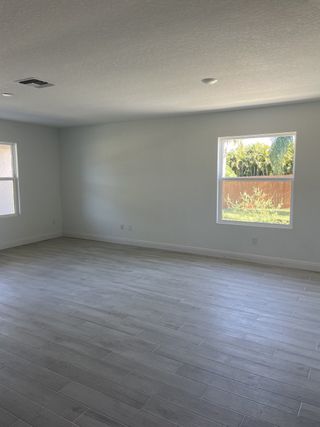 A spacious room with light wood flooring, neutral walls, and large windows offering plenty of natural light.