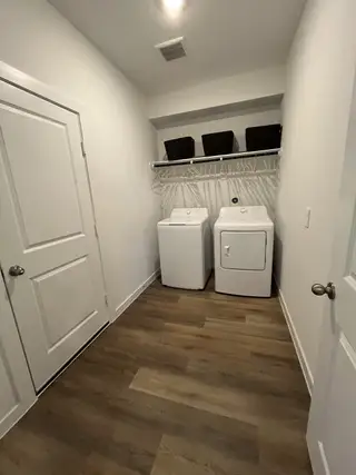 A functional laundry room with modern appliances, wood flooring, and ample shelving for organization.