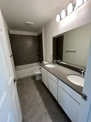 A modern bathroom with a double vanity, dark quartz countertops, and a tiled bathtub, blending style with functionality.