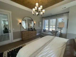A cozy bedroom featuring a chic round mirror, elegant chandelier, and inviting window seat with plush cushions.