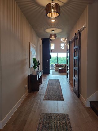 Model Home A modern hallway featuring sleek lighting, hardwood floors, and a barn door, leading to a bright living area.