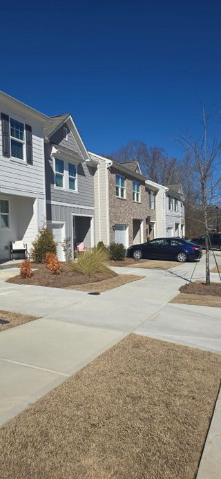 A row of stylish townhomes featuring a mix of brick and siding exteriors with driveways and a parked car.