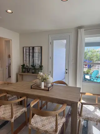 Model Home A cozy dining area with a wooden table, woven chairs, and modern decor, enhanced by natural light through large windows.