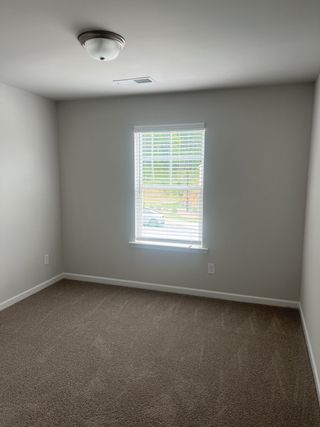 A bright room with soft carpet, neutral walls, and a window with blinds for natural light.