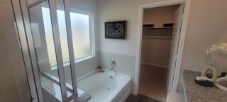 Model Home A bright bathroom featuring a spacious tub, granite counters, frosted window, and cozy adjacent walk-in closet.