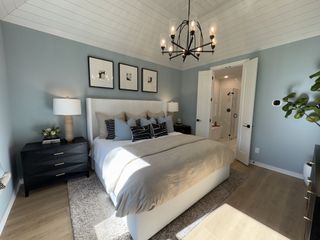A cozy bedroom with a plush bed, chic chandelier, dark wood accents, and soft lighting, opening to a modern ensuite bathroom.