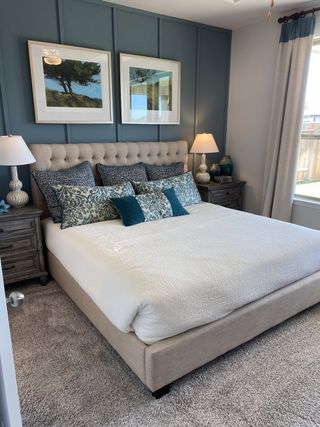 Model Home A cozy bedroom featuring a tufted bed, textured accent wall, elegant lamps, and tasteful artwork for a serene retreat.