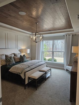 Model Home A cozy bedroom featuring a tray ceiling with wood accents, large window, soft lighting, and elegant bedding.