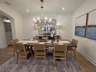 Model Home A chic dining room with a wooden table, woven chairs, and elegant lighting, accented by modern artwork and decor pieces.