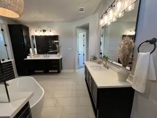 Model Home A modern bathroom featuring sleek black vanities, dual sinks, elegant pendant lighting, and a freestanding bathtub.