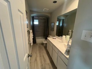 A narrow bathroom featuring a large mirror, sleek white vanity, and wood-style flooring for a modern touch.