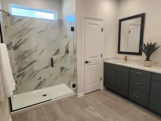 A modern bathroom featuring a marble-tiled shower, sleek green vanity, and elegant fixtures.
