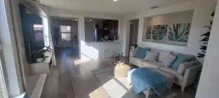 A bright living area in a Medina Crossing home, featuring a comfortable sofa with blue pillows, framed succulent artwork, and an open layout leading to the kitchen (Von Ormy, TX).