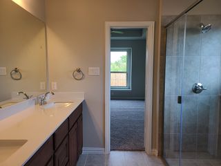 Modern bathroom featuring a sleek shower, dual vanity, and large mirror, leading to a carpeted room with a large window.