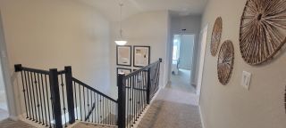 Model Home A contemporary hallway with a stylish railing, abstract artwork, and natural woven wall decor. Carpeted floors add warmth.