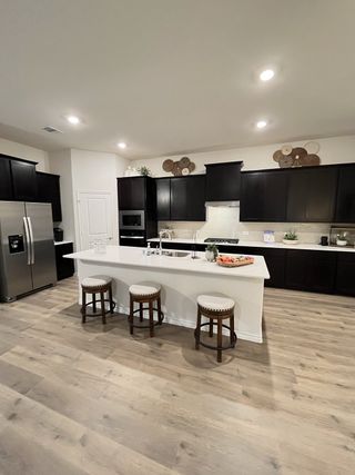 Model Home A modern kitchen with dark cabinetry, a sleek white island, and bar stools, set on elegant light wood flooring.