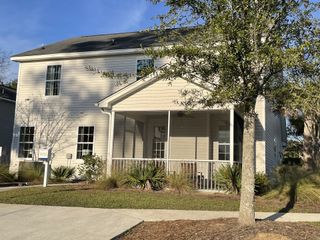 A charming beige home with a front porch and lush landscaping in High Point at Foxbank by Dream Finders Homes (Moncks Corner, SC).