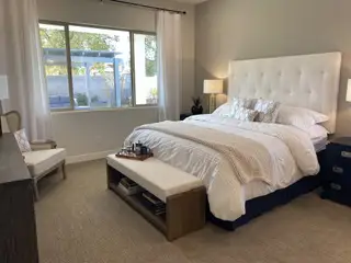 Model Home A cozy bedroom with a tufted headboard, neutral tones, large window, and elegant decor.