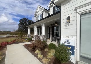 Street view A charming white home with stone accents and a welcoming porch in Harmony by Eastwood Homes (Harrisburg, NC).