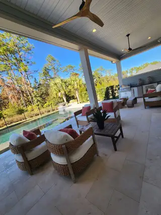 An inviting outdoor patio with comfortable seating, ceiling fans, and a view of a tranquil backyard and pool.