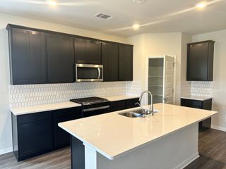 Model Home A modern kitchen featuring dark cabinetry, a sleek island, honeycomb tile backsplash, and stainless steel appliances.