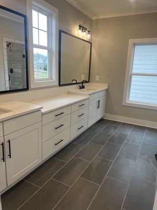 A modern bathroom with sleek gray tiles, a spacious white vanity, black fixtures, and large mirrors for a contemporary look.