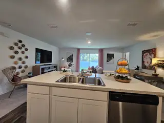 An open-concept kitchen and living area with modern decor, featuring a large window, wall accents, and cozy seating.