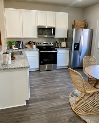 A modern kitchen featuring white cabinets, granite countertops, stainless steel appliances, and chic wicker dining chairs.