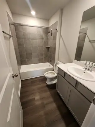 A modern bathroom featuring gray tiled walls, a sleek bathtub, and stylish dark wood flooring.