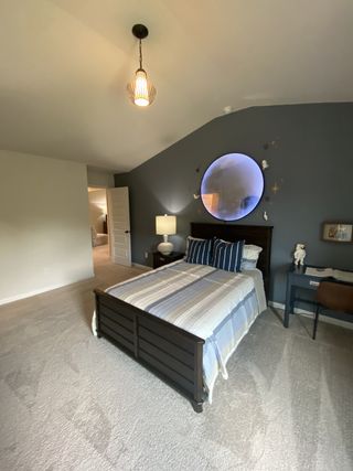 A cozy bedroom featuring a dark wooden bed, striped bedding, accent wall, and modern lighting.