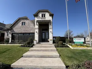 A grand model home exterior with stone and brick finishes, lush landscaping, and an inviting entryway in Solterra by Chesmar Homes (Mesquite, TX).