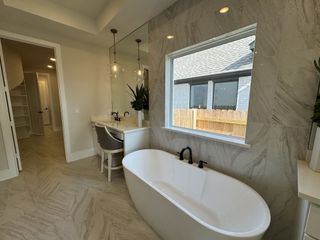 A modern bathroom with a freestanding tub, elegant vanity, and pendant lighting against marble walls.