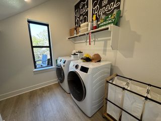 Model Home A modern laundry room with sleek appliances, wood flooring, and natural light from a large window.