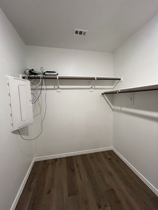A spacious walk-in closet with sleek wooden flooring and ample shelving, perfect for organized storage.