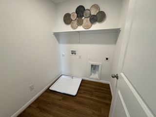 A utility closet with wood flooring, artwork, and wall hookups for appliances.