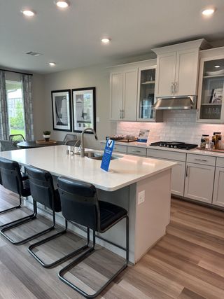 Model Home A modern kitchen featuring a sleek island, black chairs, white cabinetry, and elegant lighting.