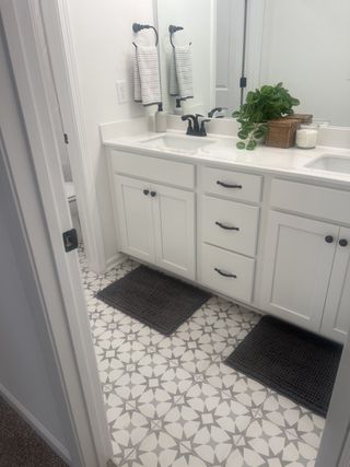 A chic bathroom with patterned tile flooring, dual sinks, sleek black fixtures, and elegant white cabinetry.
