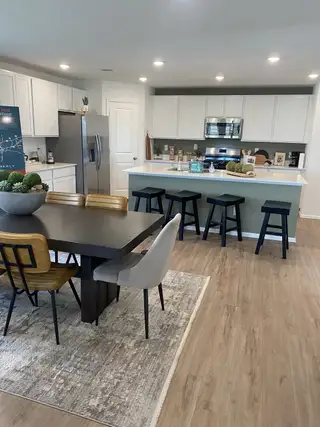 A modern kitchen with white cabinetry, stainless steel appliances, and a sleek dining area on light wood flooring.