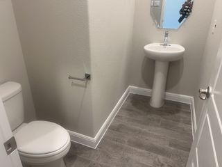 A compact powder room with a pedestal sink, modern fixtures, and wood-patterned flooring.