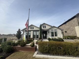 A charming single-story home in Salerno by KB Home (Round Rock, TX) features a light grey exterior, a flagpole with the US flag, and well-maintained landscaping.