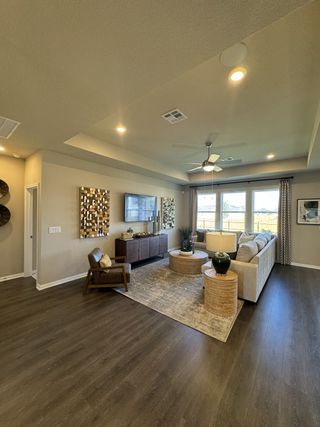A cozy living room featuring dark wood flooring, a tray ceiling, and stylish décor, with large windows inviting natural light.